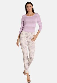 Lila gestrickter Pullover mit einem gerippten Design, kombiniert mit hellen, floral bedruckten Hosen in Lila- und Beigetönen. Schwarze Riemchensandalen.