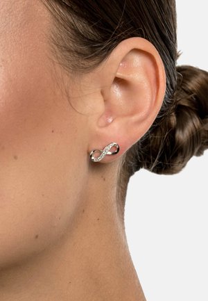 Silver infinity-shaped earring featuring a smooth, shiny finish with embedded clear crystals along one side. Worn in a pierced ear.