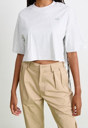 Hellgrau geschnittenes T-Shirt mit kurzen Ärmeln, rundem Ausschnitt und einem kleinen gestickten Logo auf der Brust, kombiniert mit beigen, gefalteten Hose.