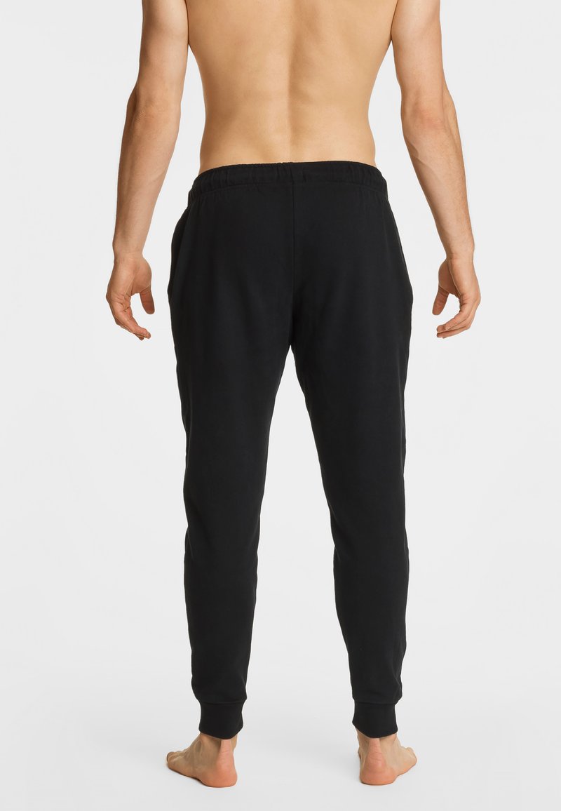 Czarne dresy z elastycznym pasem, zwężanymi nogawkami i bocznymi kieszeniami, prezentowane z tyłu na bosej postaci.