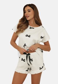 Biały bawełniany zestaw piżamowy składający się z koszulki z czarnym nadrukiem w kokardki oraz pasujących szortów z falbaniastym dołem i czarnym sznurkiem.