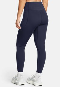 Granatowe legginsy z wysokim stanem, z płaskimi szwami, wykonane z elastycznego materiału. Posiadają tylną kieszeń i dopasowany krój. W połączeniu z białymi sneakersami.