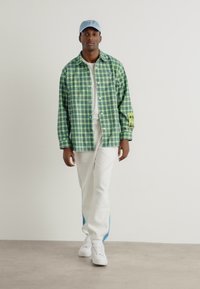 Grøn og blå ternet skjorte over en hvid T-shirt, parret med hvide bukser med blå striber og hvide sneakers.