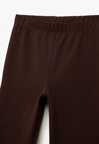 Bruna leggings gjorda av stretchigt tyg med elastisk midja och en slät, matt yta. Inga mönster eller ytterligare hårdvara synlig.
