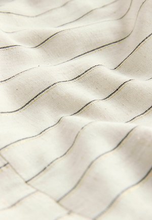 Valge kangas, millel on lainelised mustad ja kuldsed triibud, tekstuuriga pinnaga, millel on pehme, voolav välimus ja looduslikud kiud.