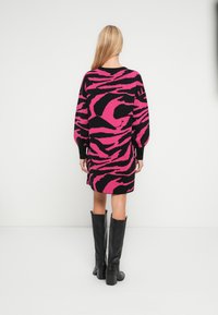 Πλεκτό φόρεμα με έντονο ρόζ και μαύρο μοτίβο ζέβρας, άνετη εφαρμογή, χαμηλωμένοι ώμοι και ριμπ μανσέτες, συνδυασμένο με μαύρες μπότες μέχρι το γόνατο.