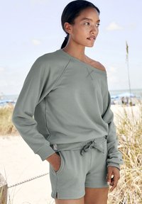Ljust grön sweatshirt med off-shoulder-design och ribbade ärmslut, kombinerad med matchande shorts med dragsko i midjan och sidofickor.