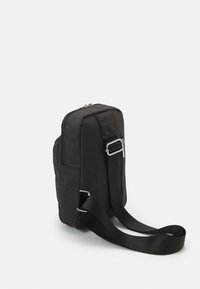 Borsa a tracolla in tessuto nero con forma rettangolare, chiusura con zip, tracolla regolabile e texture liscia. Presenta una tasca laterale con accessori.