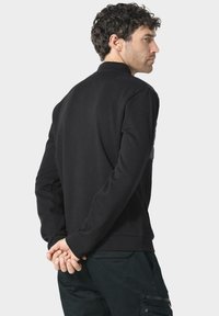Sudadera negra con textura suave, puños de canalé y cuello alto; presenta un diseño minimalista y un ajuste ceñido.