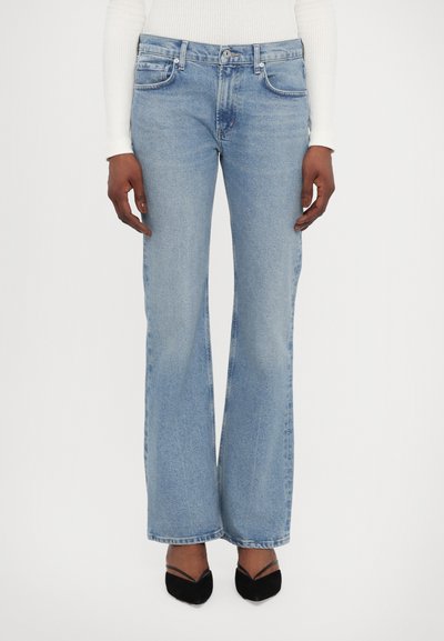 Lichtblauwe wijde jeans met een mediumhoge taille, voorzakken en een vervaagde textuur. Draagt met zwarte puntige schoenen.