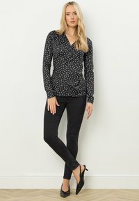 Zwarte lange mouw top met witte stippen, strakke pasvorm, gecombineerd met zwarte skinny jeans en zwarte puntige hakken. Eenvoudige en gladde textuur.