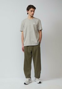 Grijze katoenen t-shirt met korte mouwen, voorzien van een klein wit logo, gecombineerd met losse olijfgroene broeken en witte sneakers.