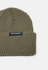 Grön ribbstickad mössa med vikbar kant. Har en svart etikett med varumärket i vit text. Mjukt material.