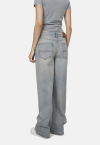 Jasnoniebieskie dżinsy o szerokich nogawkach, wykonane z denimu. Posiadają wysoki stan, tylne kieszenie oraz brązową skórzaną metkę na pasku.