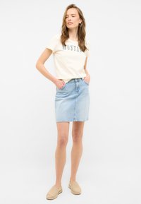 Gonna di jeans leggera con taglio dritto, lunghezza a metà coscia. Abbinata a una t-shirt crema con design stampato. Scarpe beige senza lacci.