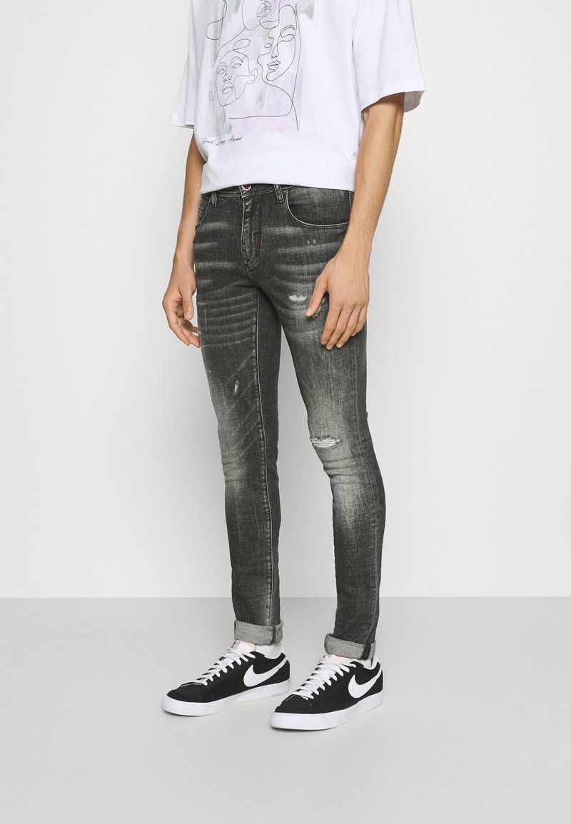 Jeans ajustados de color negro deslavado con ligeras desgastadas, combinados con dobladillos enrollados, junto con zapatillas Nike en blanco y negro y una camiseta gráfica blanca.