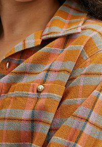 Orange and gray plaid shirt with a textured fabric, featuring a button on the pocket and a collared neckline.