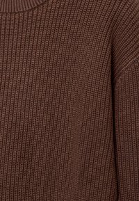 Ruskea neulottu villapaita, jossa on teksturoitu ribbikuvio, pyöreä pääntie ja rento, hieman lasketut olkapäät.