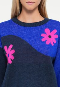 Knit sweater in blue and dark navy with floral design, featuring two pink flowers. Round neck with textured finishes.