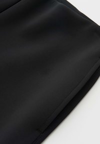 Schwarzer Stoff mit glatter, matter Textur, klaren Kanten und minimalen Nähten. Das Material zeigt unter Licht leichtes Glänzen.