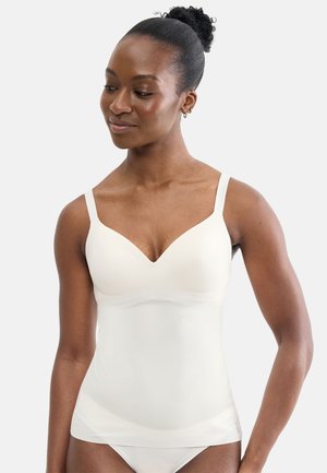 Woman with dark skin and curly hair in a bun wearing a white fitted camisole and matching underwear, looking slightly down and to her right.