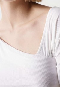 Top bianco a coste con scollatura ampia e maniche corte, realizzato in tessuto morbido e texture, con leggera arricciatura sulla cucitura della spalla.