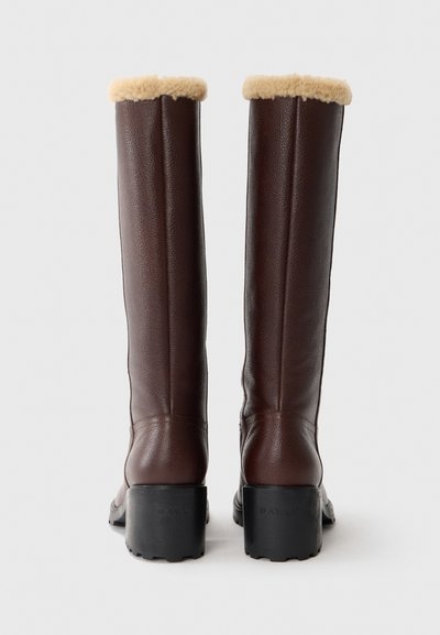 Brown leather knee-high boots with a plush beige trim at the top and a chunky black heel. The design features subtle stitching details.