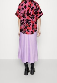 Camicia a maniche corte con un motivo floreale rosa e nero, abbinata a una lunga gonna lavanda e stivali neri con tacco.