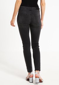 Mustat tiukat farkut, joissa on korkea vyötärö, viisi taskua ja hienovarainen kulutuskuvio etuosassa. Kangas näyttää joustavalta ja siinä on sileä pinta.