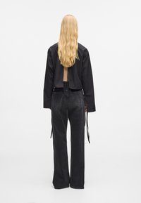 Svart kortet skjorte med åpen rygg, parret med høyt liv svarte denimjeans med løs passform og lange stropper på sidene.