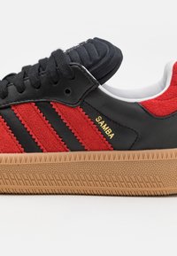 Svart lær sneakers med røde semskede striper, med gummisåle og "SAMBA" gull detaljer. Rund tå og strukturert tunge.