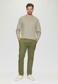 Felpa beige chiaro con maniche lunghe, abbinata a pantaloni verde oliva e sneakers bianche; vestibilità casual con polsini a coste e tasche laterali.