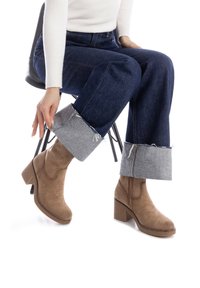 Botas de ante marrón hasta el tobillo con un tacón cuadrado, combinadas con jeans de mezclilla azul con puños enrollados y una camiseta de manga larga blanca de canalé.