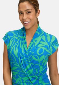 Robe à manches courtes en tissu bleu avec un motif de feuilles vertes ; présente un design enveloppant et une texture lisse.