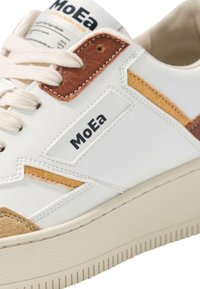 Witte sneaker met tan en bruine suède accenten, uitgerust met een gestructureerde zool, ronde veters en een logo label aan de zijkant.