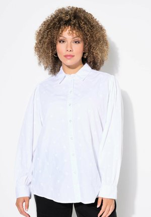 Camisa blanca de botones con patrones de corazones sutiles, mangas largas con puños fruncidos y un cuello clásico.