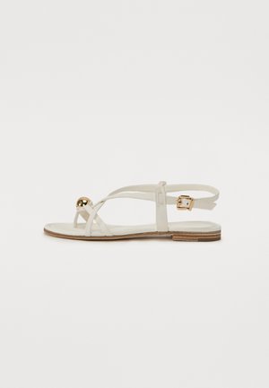 White leather sandal with thin straps, a gold decorative ball, and an adjustable ankle strap. Flat rubber sole with a wooden accent.