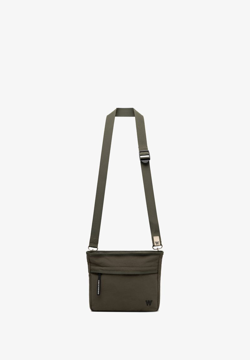 Sac bandoulière vert olive en tissu avec un design structuré, comportant une fermeture zippée, une poche avant et une bandoulière réglable.