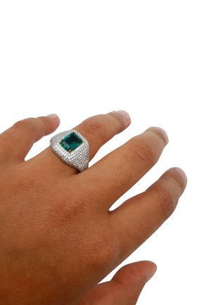 Anello in argento con finitura testurizzata, caratterizzato da un gemma verde quadrata, fissata con quattro griffe dorate, indossato su una mano dalla tonalità della pelle naturale.