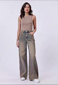 Beige ribbed tank top paired with high-waisted, wide-leg faded jeans featuring a braided belt and white sneakers. Smooth texture, casual design.