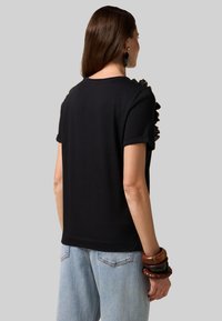 Camiseta negra de manga corta con detalle de hombros fruncidos, elaborada en una tela suave, combinada con unos vaqueros de tiro alto en azul claro.