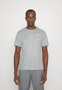 Mand iført en lysegrå Nike t-shirt med korte ærmer og matchende grå bukser, stående mod en ensfarvet hvid baggrund.