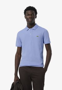 Vaaleansininen puuvillapolo-paita, jossa on kaksinappinen kaulus, lyhyet hihat ja vihreä krokotiililogo rinnassa.