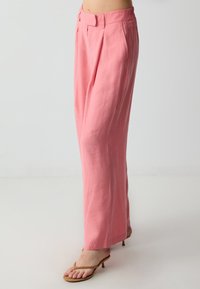 Roze linnen broek met wijde benen en een geplooide voorkant. Heeft een op maat gemaakte tailleband en een gladde textuur, gecombineerd met bruine hakken sandalen.