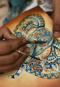 Gedetailleerde illustratie van een olifant met ingewikkelde patronen in blauw, oranje en zwart. De kunstenaar gebruikt fijne penselen op structuurpapier.