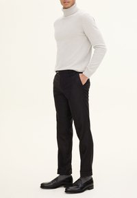 Light grey turtleneck sweater, black tailored trousers, and black leather shoes. Slim-fit design with textured fabric and rolled cuffs.