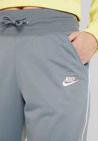 Grå sportbyxor med ribbad midja, dragsko och sidofickor. Har en vit accentrand och en rosa Nike-logga. Lättviktsmaterial.