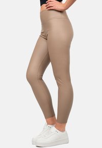 Leggings a vita alta color beige realizzati in materiale elasticizzato, con una texture liscia e cuciture a contrasto, abbinati a sneakers bianche.