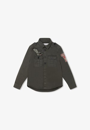 Mørkegrøn skjorte med knapper foran og lange ærmer. Har to forlommer, skulderstropper og broderede fugle- og bogstavs-mærker.