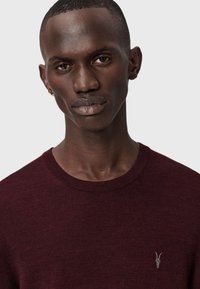 Maglione bordeaux a girocollo con un motivo a maglia testurizzato, dotato di un piccolo logo a forma di corno argentato sul petto. Design liscio e aderente.